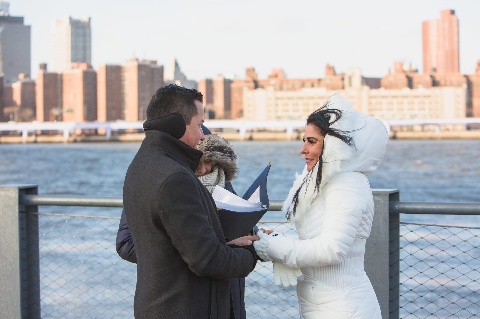 Newlyweds celebrating with arms raised, Manhattan skyline behind them at Brooklyn Bridge Park